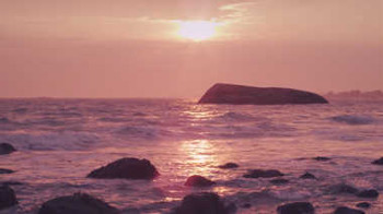 A rock in the ocean with a setting sun